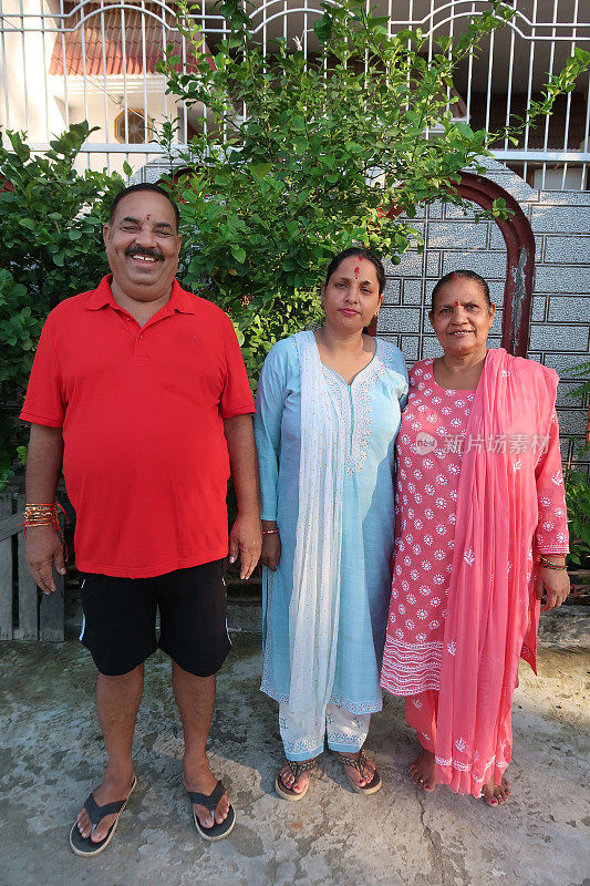 印度教徒形象，印度两代家庭，丈夫，妻子和女儿，男人穿着休闲服装，女人穿着Salwar Kameez传统服装，穿着分发的sindoor，额头上有bindi，站在铺好的院子里